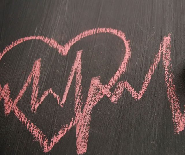 Heart with heartbeats drawn with chalk on wooden background